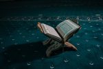 A closeup of an opened holy book of Quran put on a wooden pedestal on a carpet