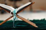 Holy Quran with prayer rosary beads on wooden stand close up