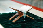 Holy Quran with prayer rosary beads on wooden stand close up